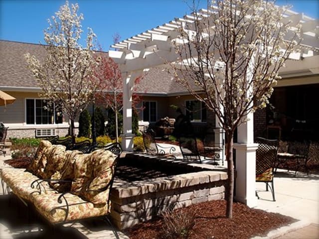 A serene patio with comfortable seating and a pergola amidst landscaped surroundings.