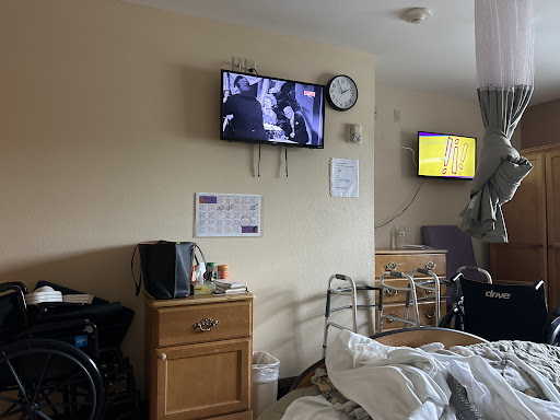 A view of a hospital room featuring a patient bed, two televisions, and various medical items.