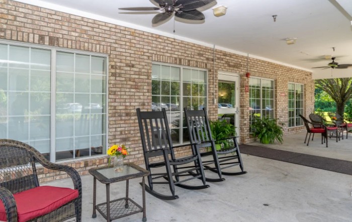 A cozy patio area with rocking chairs and a ceiling fan against a brick wall.