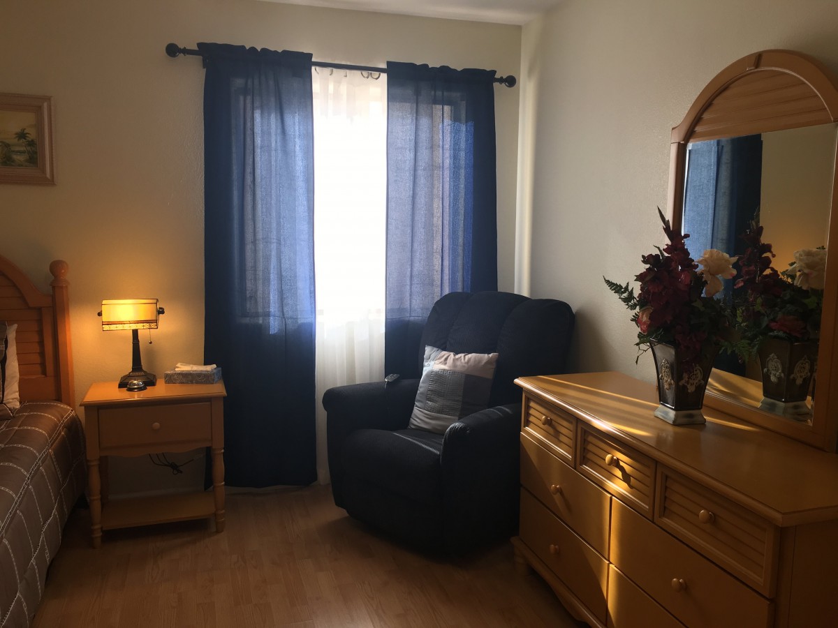 Cozy bedroom corner with a comfortable chair and wooden dresser near the window.