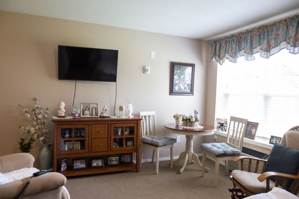 A cozy living room with a wall-mounted television, a wooden cabinet, and a small dining area by the window.