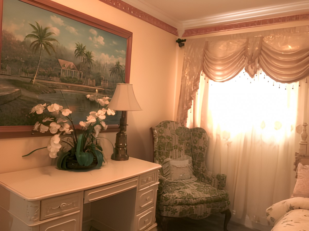 A cozy living room corner featuring a decorative chair, a lamp, and a painting above a desk with flowers.