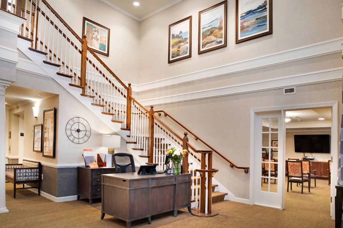 A well-lit reception area with a large staircase, a desk, and framed artwork on the wall.