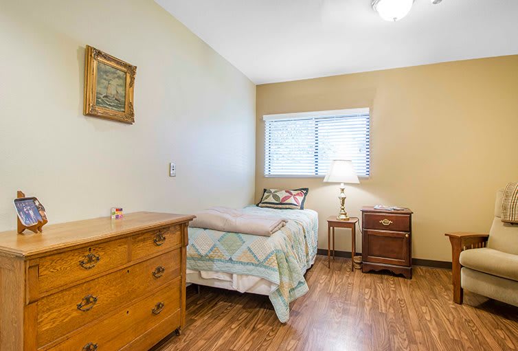 A cozy bedroom with a single bed, wooden furniture, and a small window letting in natural light.