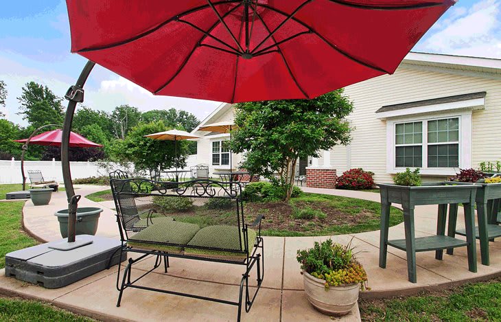 A cozy patio area featuring a red umbrella, lush greenery, and comfortable outdoor seating.