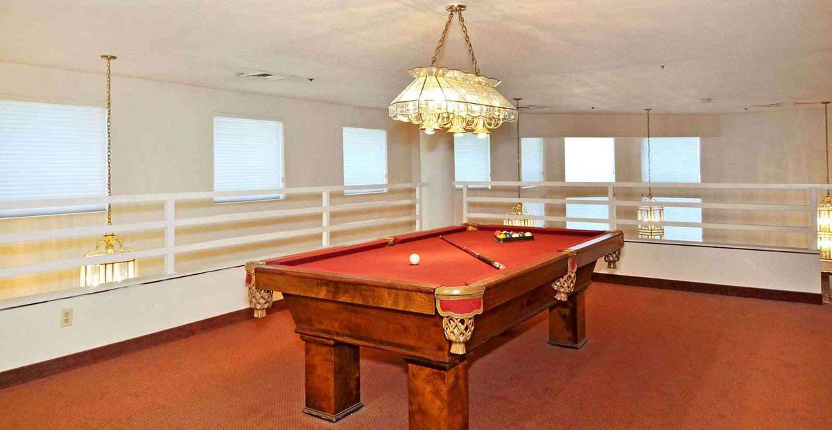 A well-lit game room featuring a red felt pool table under a decorative chandelier.
