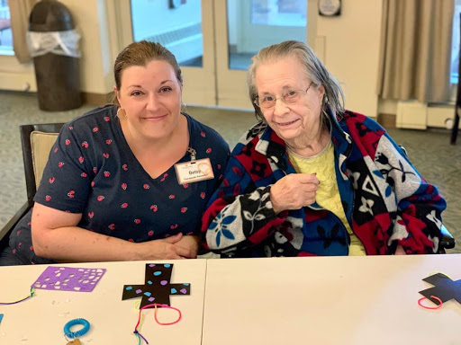 A caregiver and an elderly woman smiling together during a crafting session.