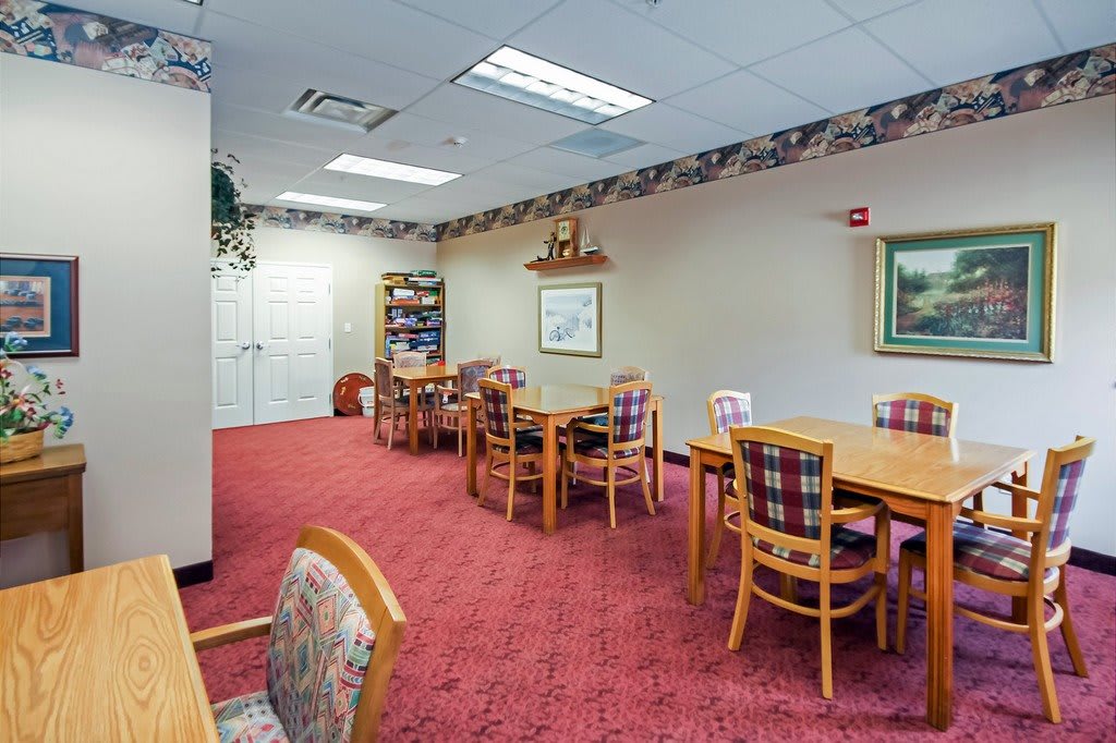 A cozy dining area with multiple tables and chairs, featuring a warm carpet and decorative lighting.