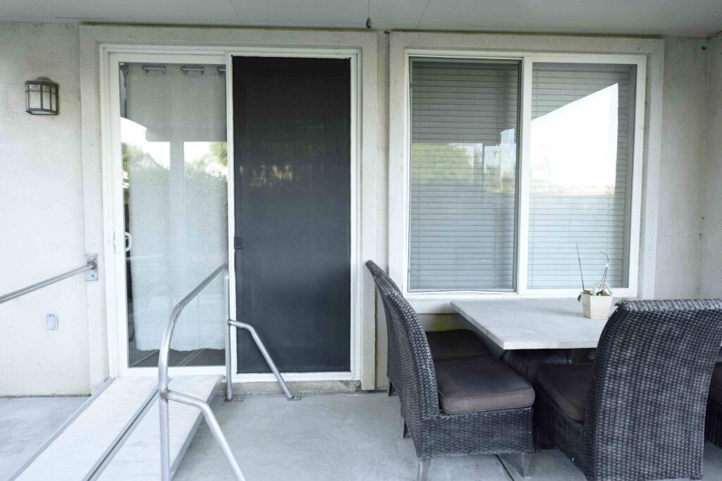 A patio area with a table and chairs next to a sliding glass door and windows.