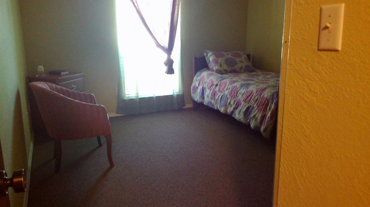 A simple bedroom with a single bed and chair beside a curtained window.