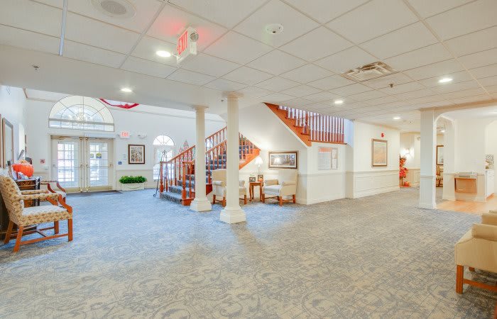 A spacious and well-lit lobby area featuring a staircase, carpeted floors, and various pieces of furniture.