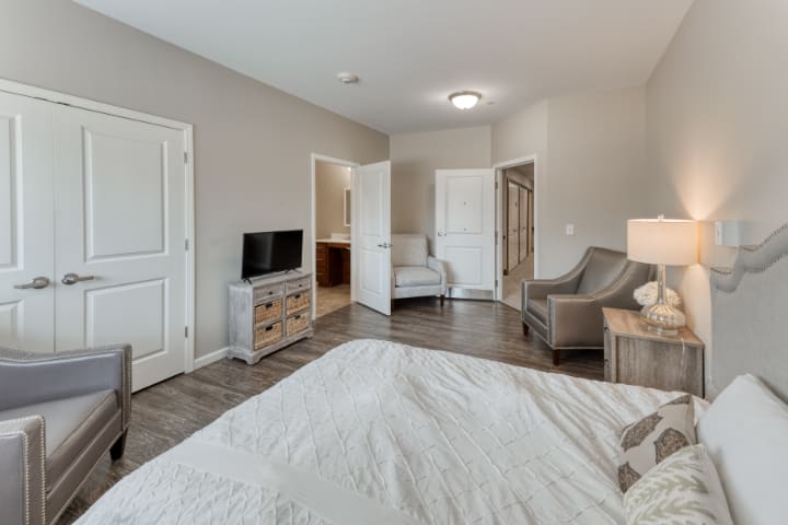 A modern bedroom featuring a TV, comfortable seating, and wooden flooring.