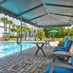 A relaxing outdoor area featuring a swimming pool with lounge chairs and sunshades, surrounded by palm trees.