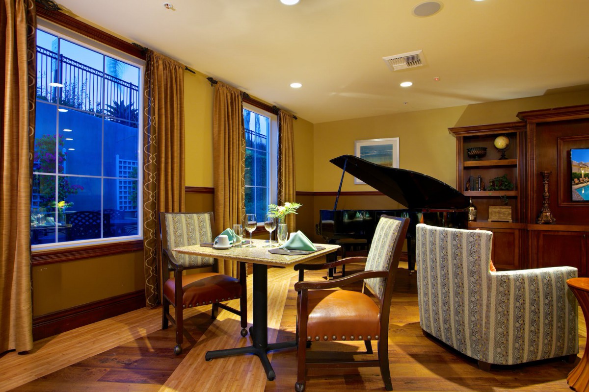 An elegant dining room featuring a grand piano and a cozy table setting by the window.