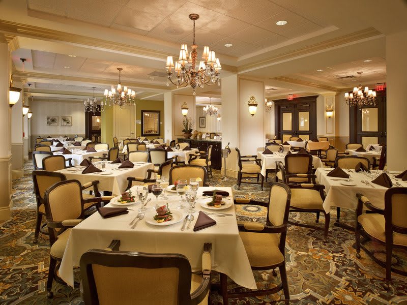 An elegant restaurant dining room with beautifully set tables and luxurious chandeliers.