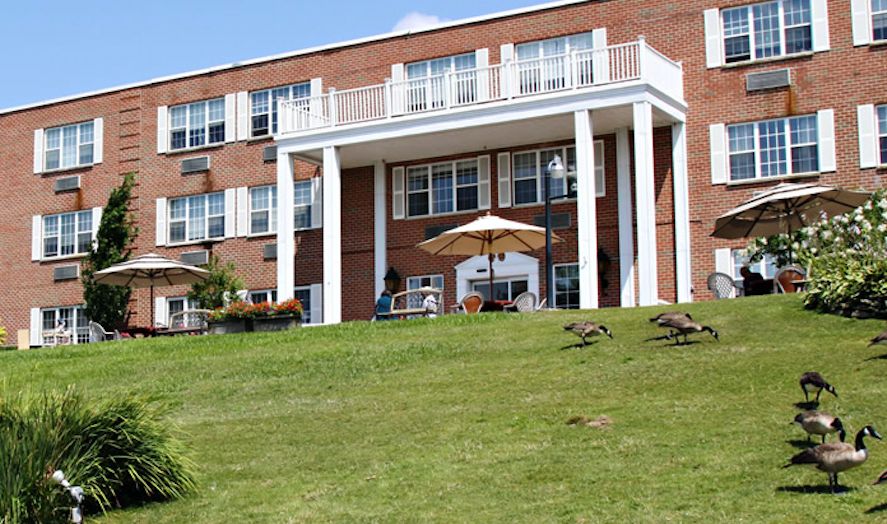 A multi-story brick building with a spacious lawn and a patio featuring an umbrella.