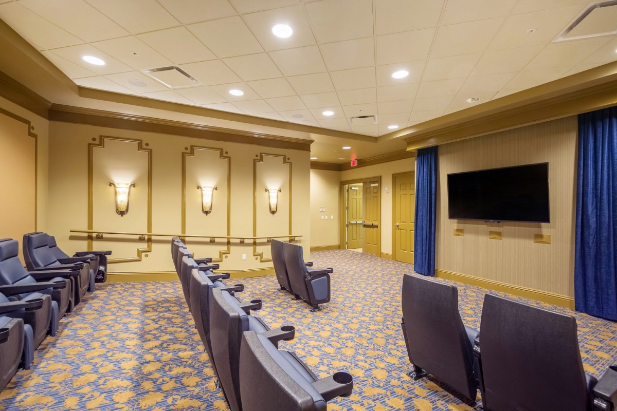 An interior view of a small theater with rows of seating and a wall-mounted screen.