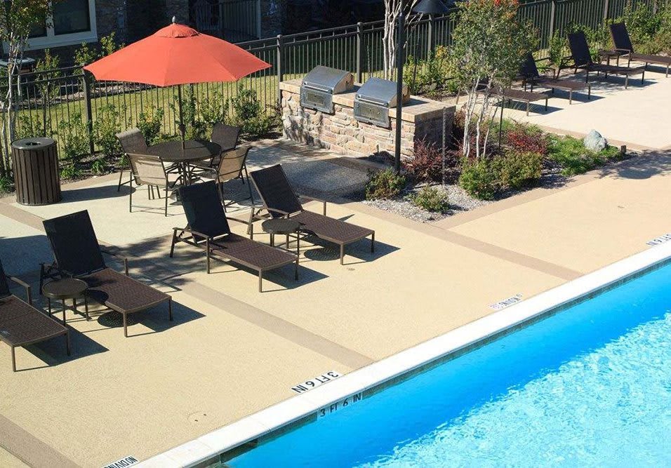 A sunny outdoor area featuring a swimming pool, lounge chairs, and a patio with an umbrella.