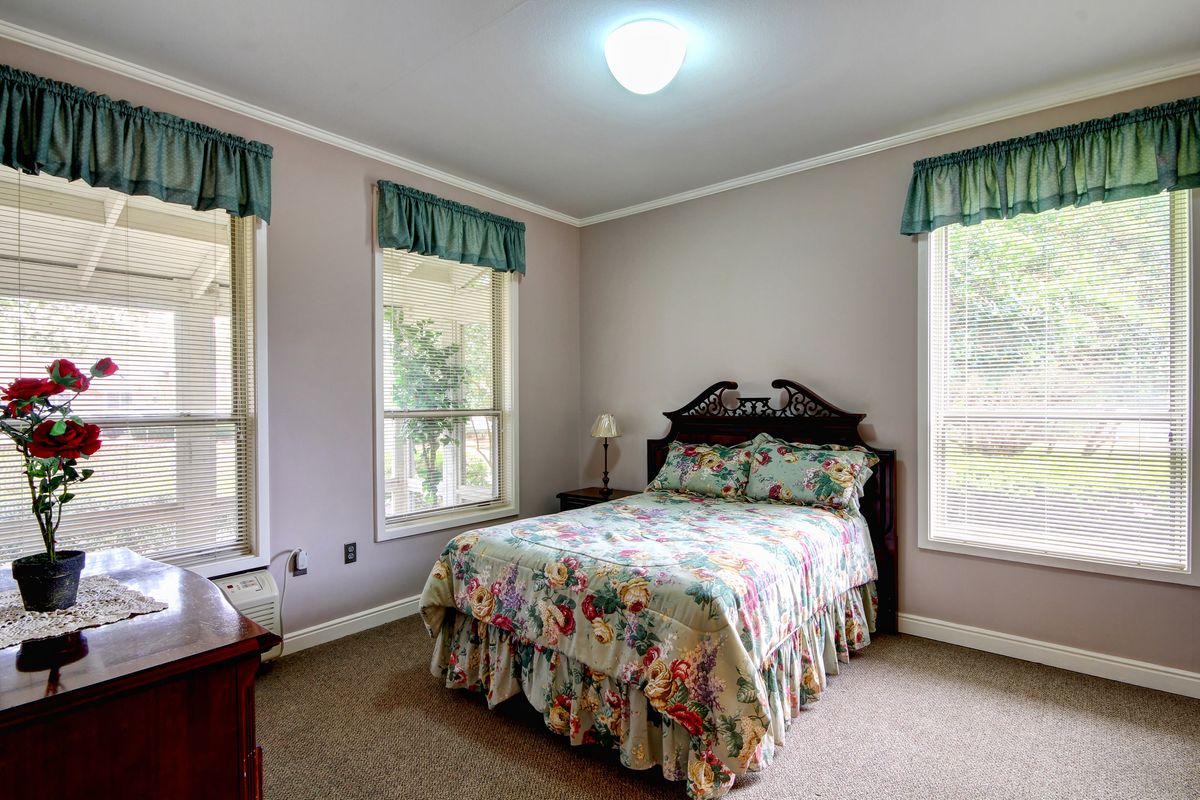 A cozy bedroom featuring a floral bedspread, two windows with valances, and a small bedside lamp.