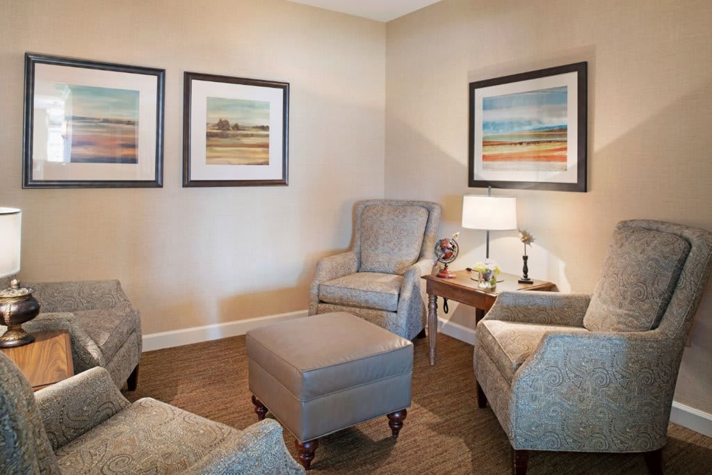 A cozy living room with armchairs, an ottoman, and framed artwork on the walls.