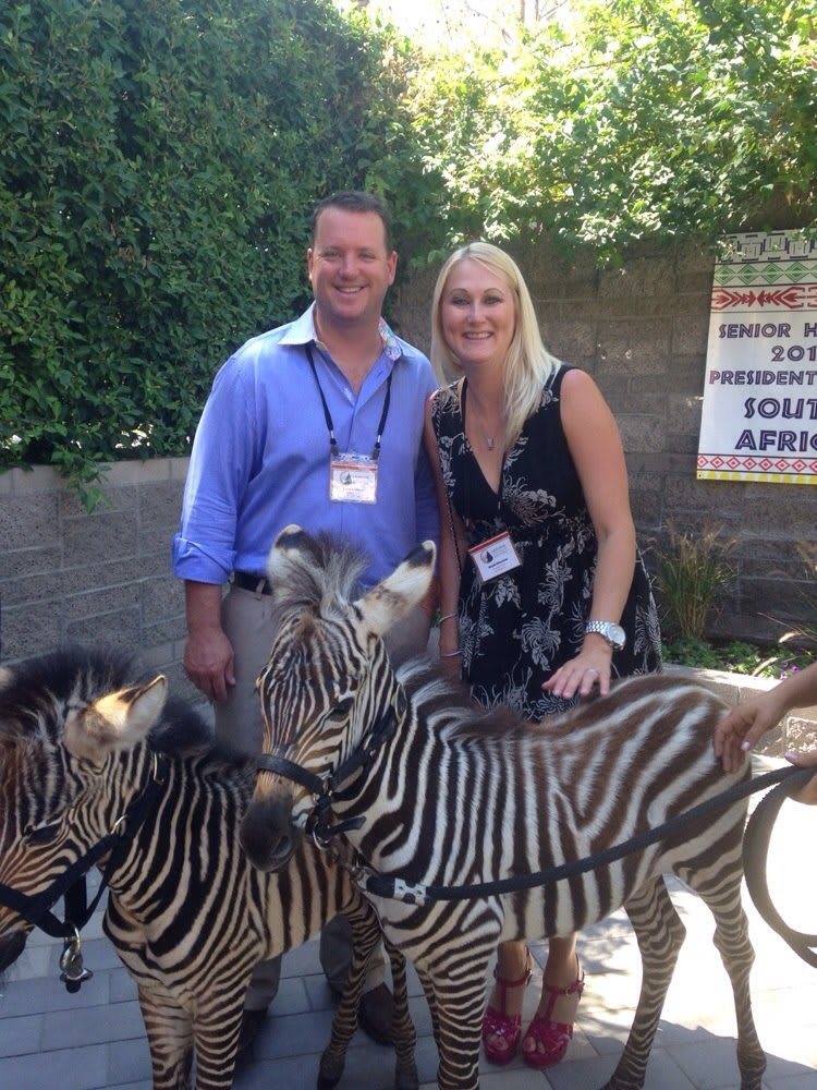 A smiling couple poses with zebras in an outdoor setting.