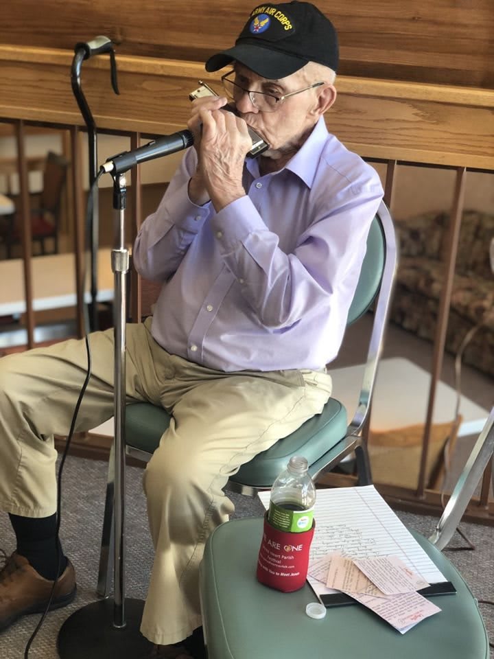 A senior musician playing the harmonica while seated and using a microphone.