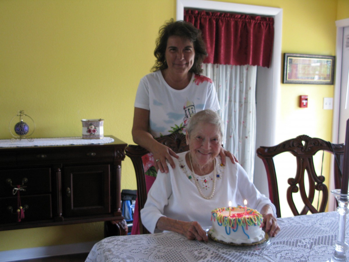 An elderly woman celebrates her birthday with a cake and candles, accompanied by a family member.