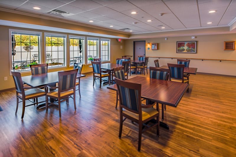 A spacious dining area with wooden tables and chairs, featuring large windows and a well-lit atmosphere.