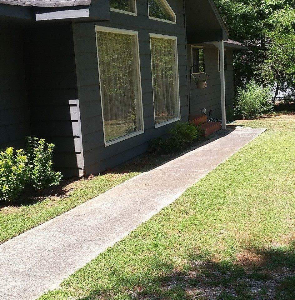 A view of a house exterior with large windows, a grassy yard, and a concrete pathway.