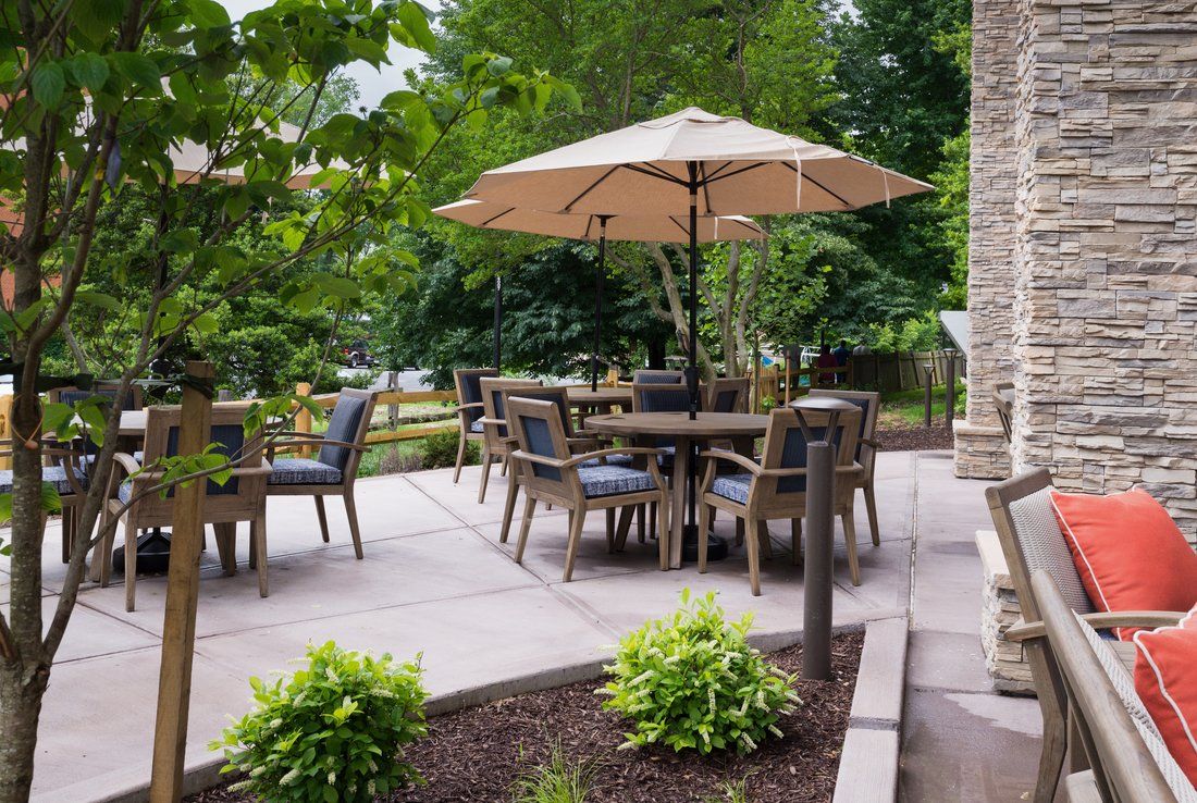 A serene patio setting with outdoor furniture and umbrella, surrounded by lush greenery.