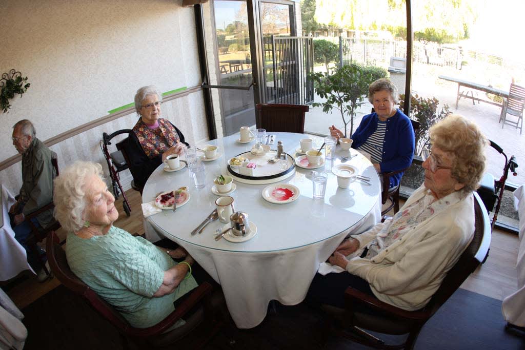 A group of elderly individuals enjoying a meal together around a table with a cake in the center.