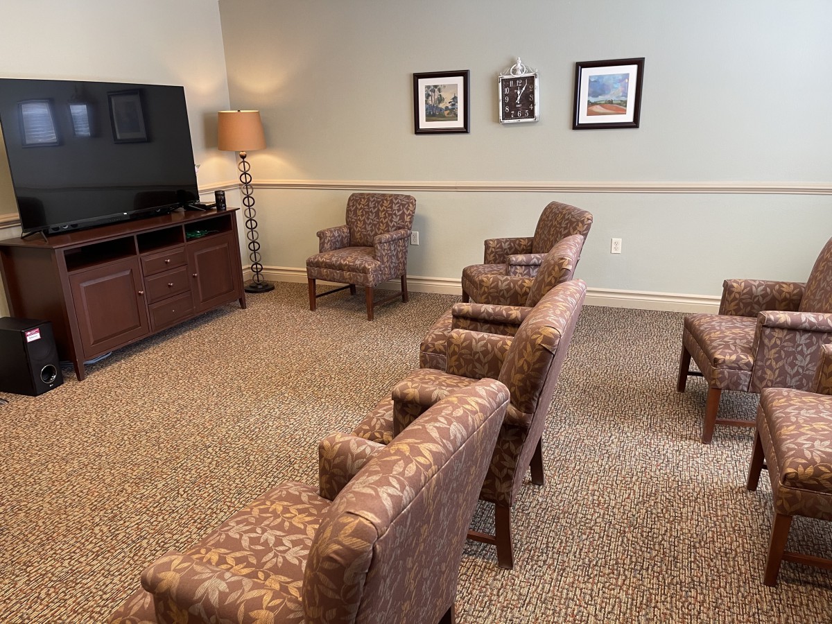 A cozy waiting room with arranged chairs facing a television and framed pictures on the wall.