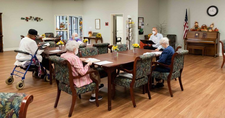 A group of senior citizens engaged in a reading activity at a nursing home community room.
