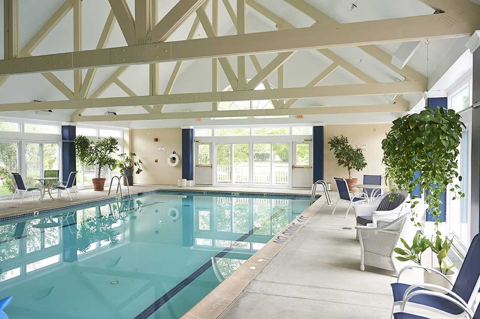 A well-lit indoor swimming pool area with comfortable seating and lush plants.