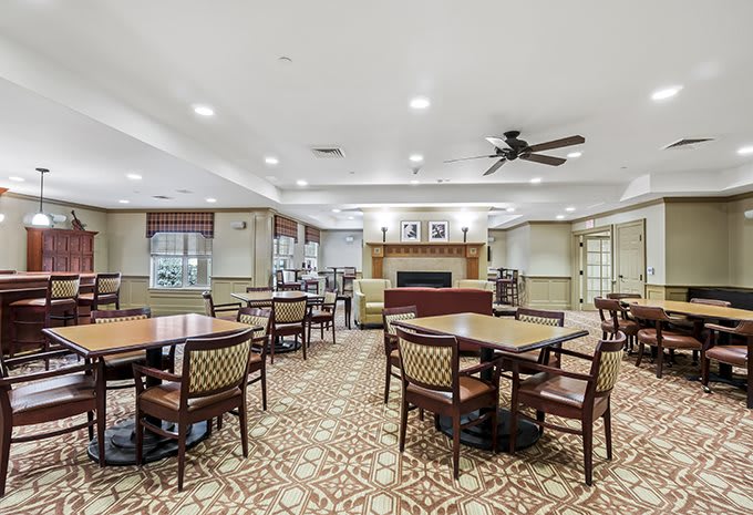 Spacious dining area with multiple tables and chairs, featuring a fireplace and ceiling fan.
