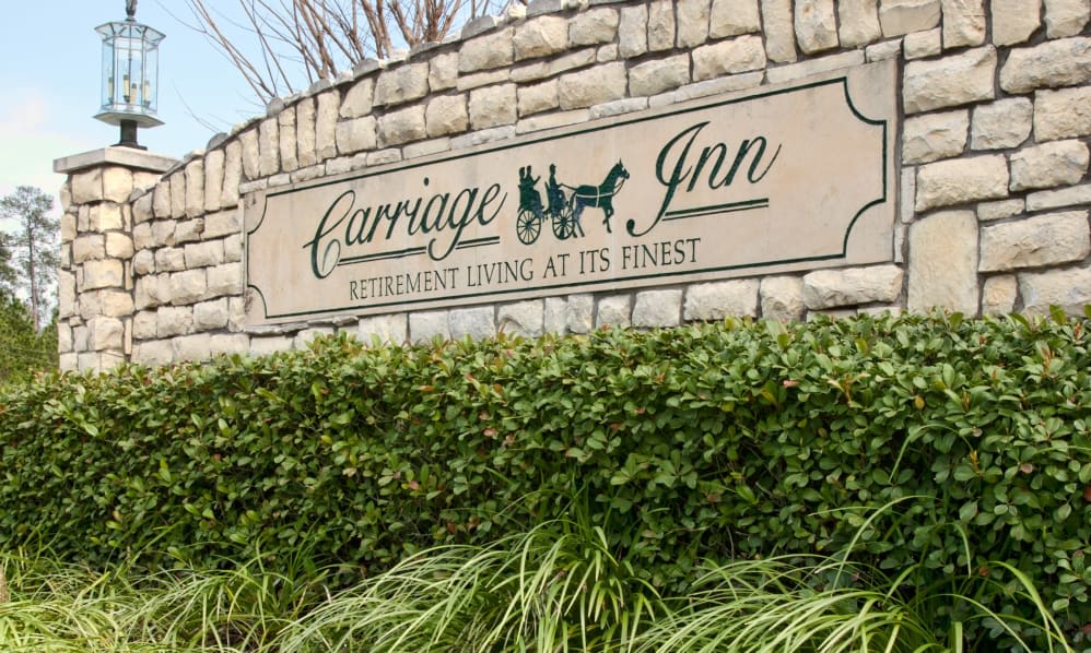 Entrance sign for Carriage Inn Retirement Living surrounded by greenery.