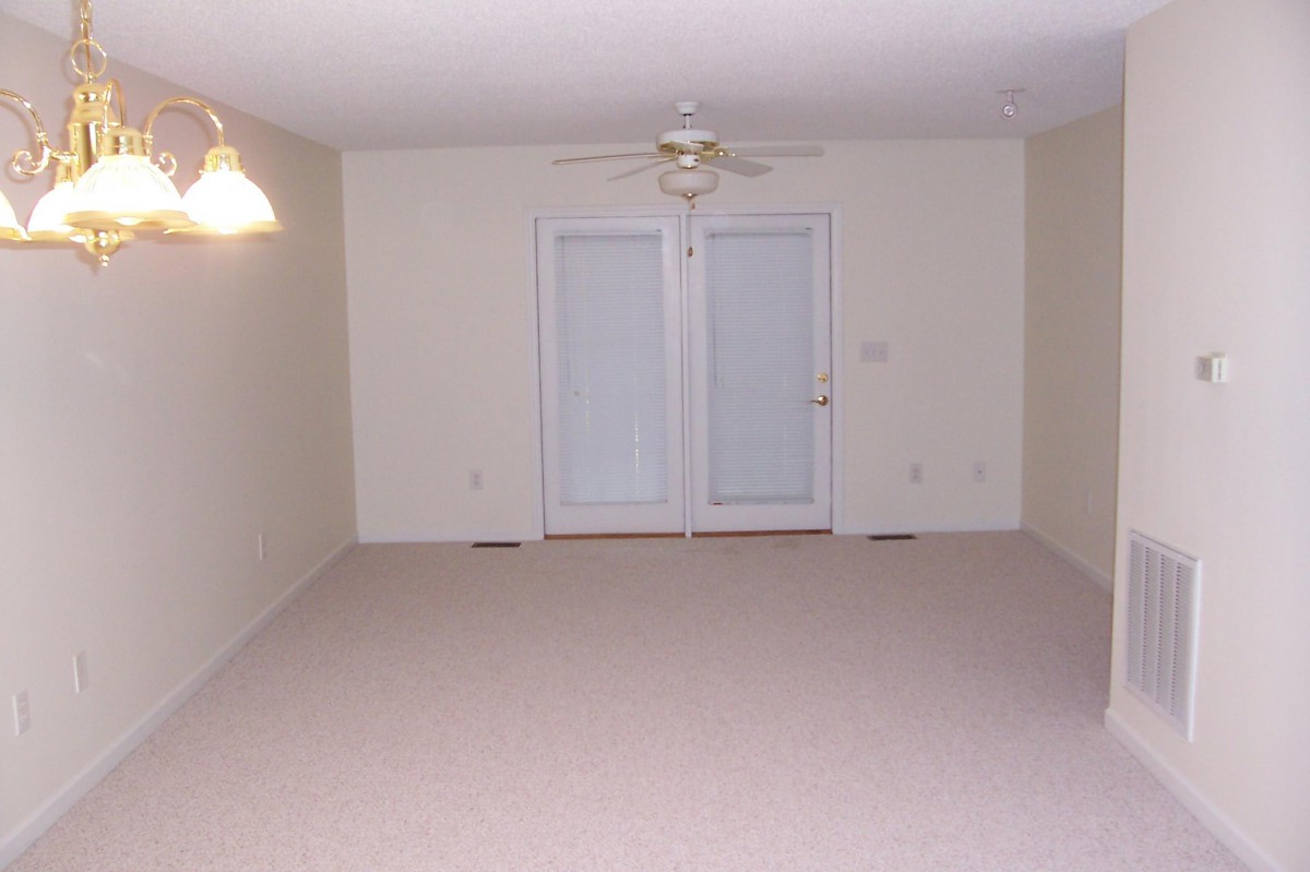 An empty room with carpet flooring, a ceiling fan, and French doors leading outside.