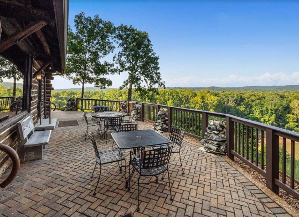 A scenic outdoor patio with tables and chairs overlooking a lush forested area.