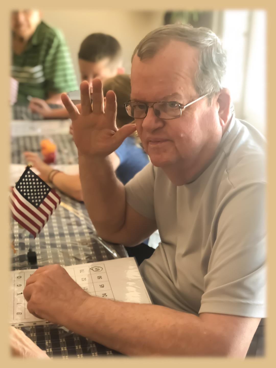 A man with glasses sitting at a table holding a small American flag while working on papers.