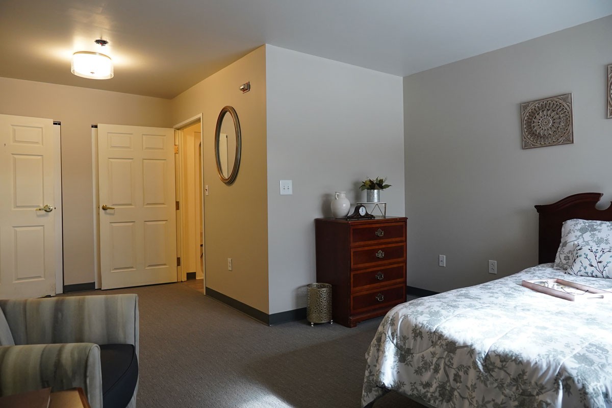 A cozy bedroom with a dresser, mirror, and a doorway leading out.