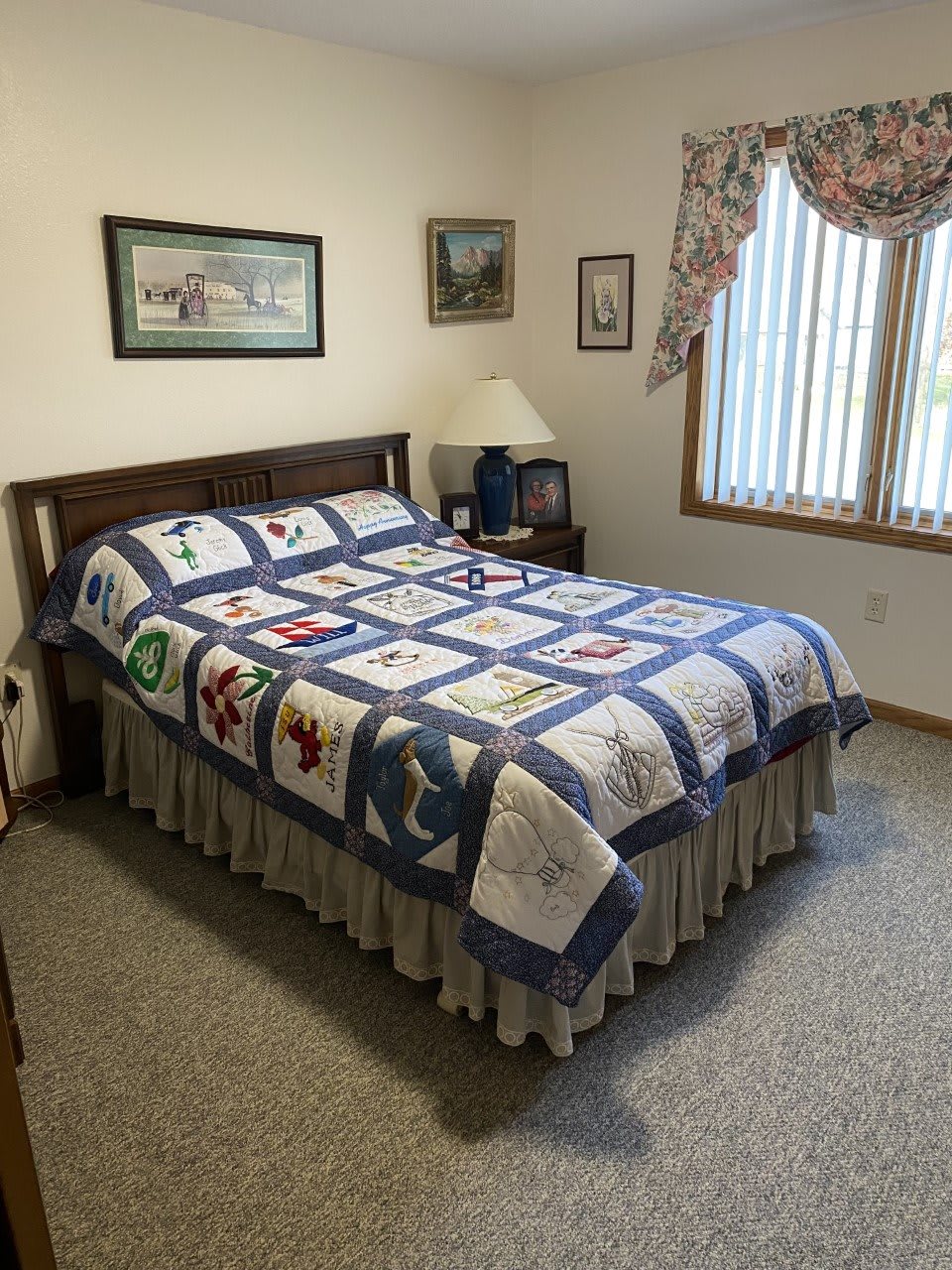 A cozy bedroom featuring a quilt-covered bed, art on the walls, and a window with curtains.