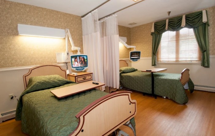 A hospital room with two patient beds separated by curtains, each equipped with a television.