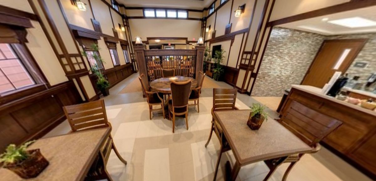 An elegantly designed restaurant interior featuring wooden tables and chairs, with decorative plants and ambient lighting.
