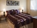 A cozy bedroom featuring a neatly made bed with a striped comforter, flanked by lamps and decorated with framed photographs on the wall.