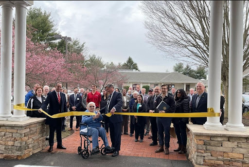 A community gathering for a ribbon-cutting ceremony, marking the opening of a new facility amidst blooming trees.