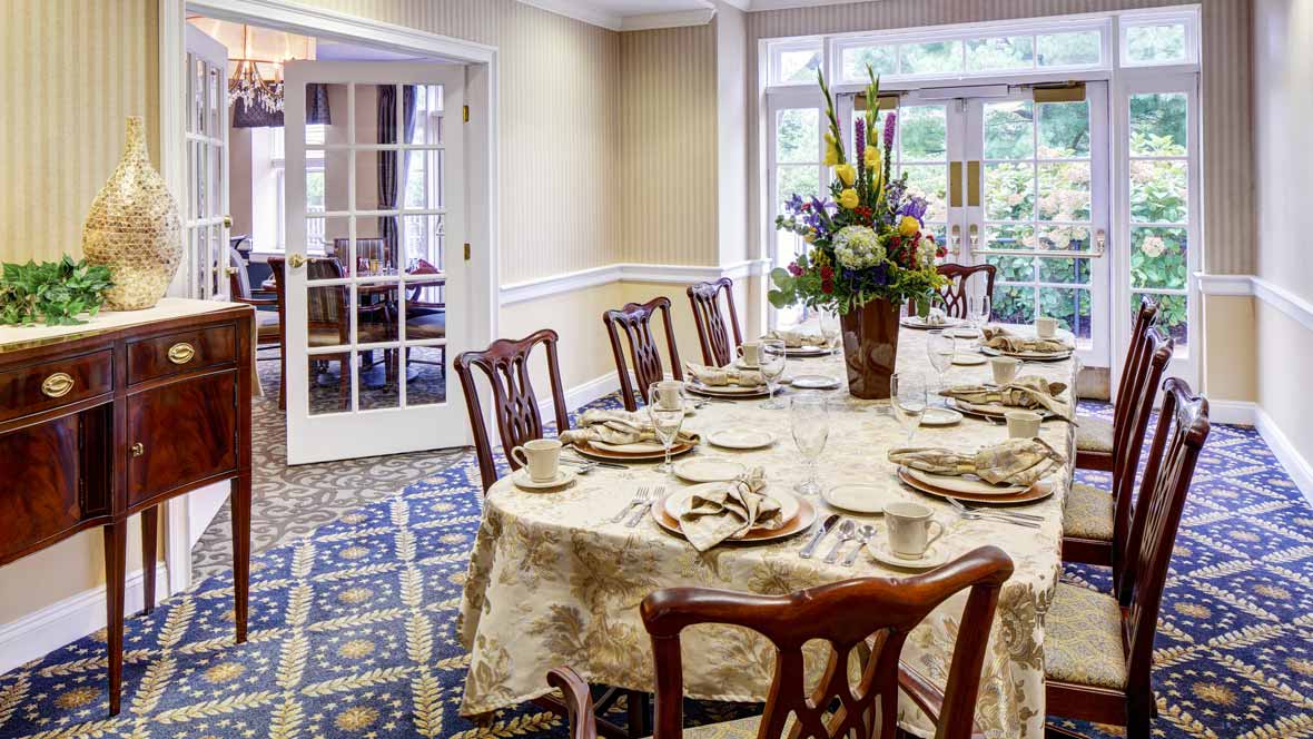 An elegantly set dining table with floral centerpiece and wooden chairs in a well-decorated room.