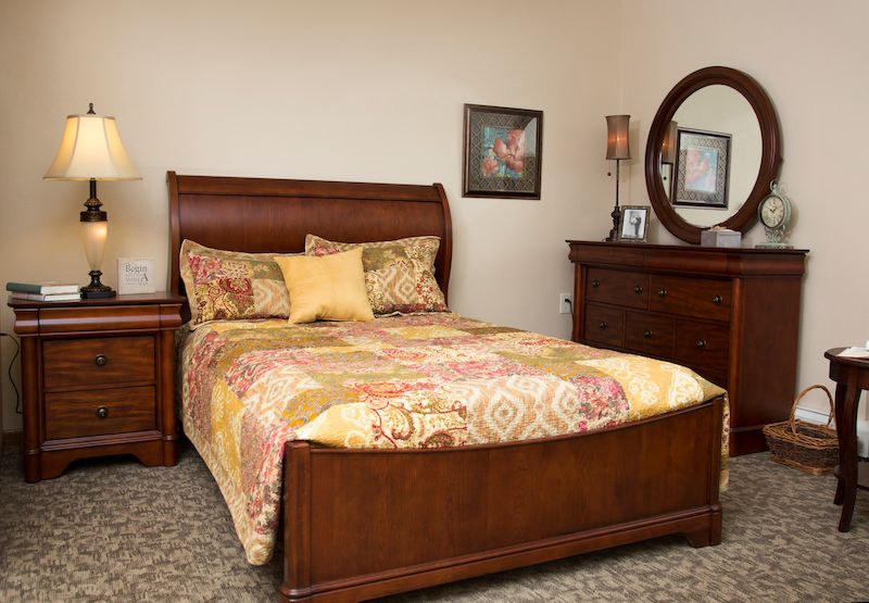 A cozy bedroom with a wooden bed frame, matching nightstand and dresser, adorned with decorative pillows.