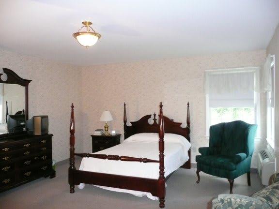 A classic-style bedroom featuring a four-poster bed, an armchair, and a dresser.