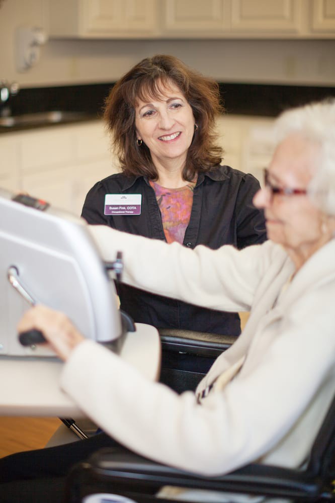A healthcare worker assisting an elderly woman with exercise equipment.