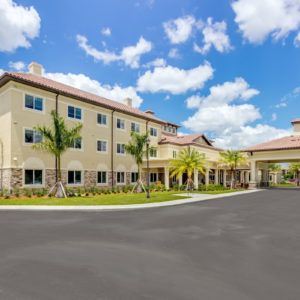 A modern building with palm trees and a driveway under a clear blue sky.